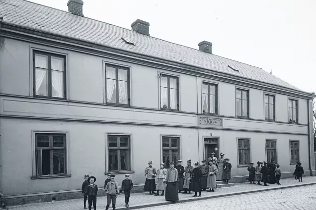 Tvåvåningsbyggnaden från 1800-talet med några människor framför. Foto.